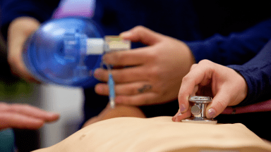 close-up of paramedics working on manikin with stethoscope and giving oxygen