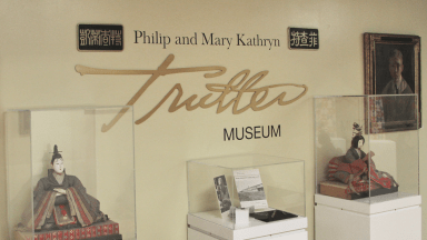 Three pieces of art in display cases in front of a wall that says Philip and Mary Kathryn Trutter Museum.