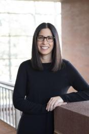 A woman in a black sweater leaning on a wall.