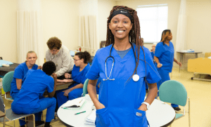 a smiling student standing in a classroom with other students behind her