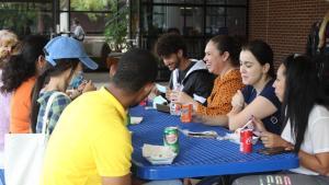 Eight students sit at a picnic bench outside Menard Hall with food and drinks while at the Multicultural Fest.