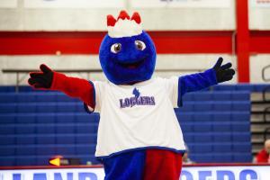Linc, the LLCC mascot, wears a Loggers jersey and gestures with two arms outstretched in Cass gym.