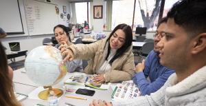 Students at table, books open and pointing at globe