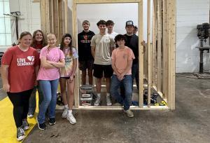 Group of eighth grade students standing in and around framed structure