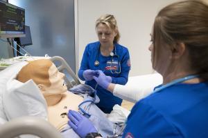 two nursing students tending to a manikin patient in a hospital bed