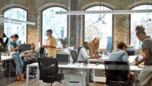 A group of people work in an office with large windows. Thre