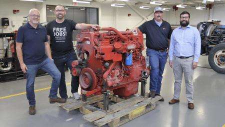 LLCC and JX Enterprises representatives stand next to a donated diesel engine.