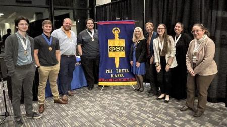Phi Theta Kappa officers and advisors pose for a photo with a large Phi Theta Kappa Alpha Epsilon Kappa banner.