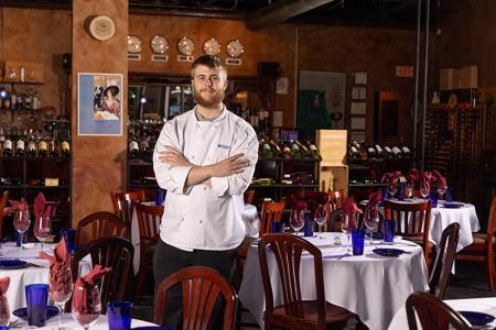 Dawson Bakunas, LLCC Culinary student, poses with arms crossed inside Indigo restaurant