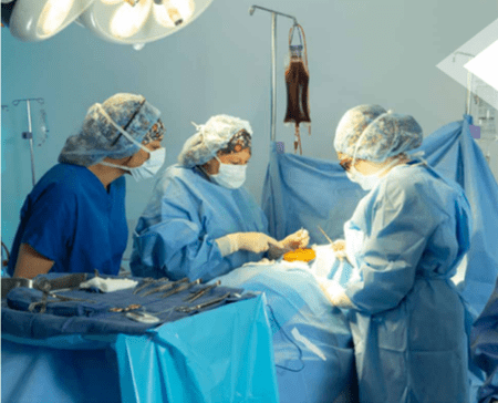 Three students in scrubs learning through surgical technology lab, surgical instruments at foot of mannequin patient