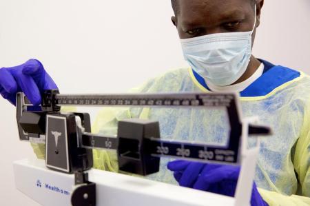 CNA student in scrubs, mask and gloves working a scale