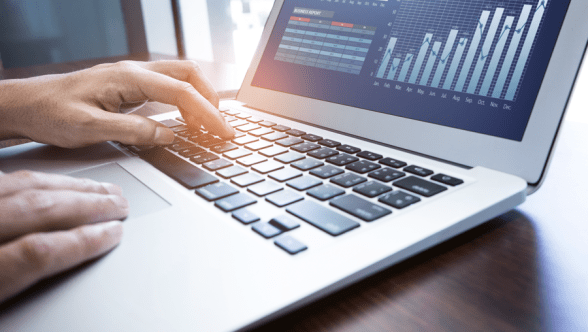 Typing on a laptop keyboard with charts on the screen.