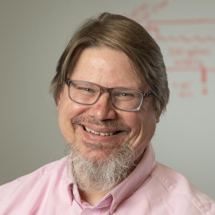 A man with gray-ish hair and glasses, wearing a light-pink colored shirt.