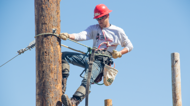 An electrical distribution lineman student climbs a pole.