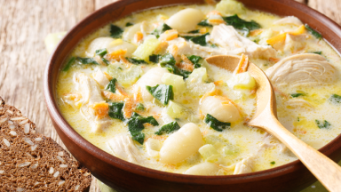 Cream soup with gnocchi, chicken and spinach served with bread close-up in a bowl.